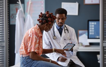 Side view of adult African American woman pointing at the screen during consultation with doctor in clinic and asking questions about treatment, copy space